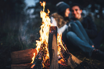 Pretty couple relaxing near bonfire in the forest at evening time