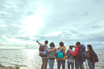 Look there. Portrait of friends standing on the beach and peering at sea. Man pointing at sun. Copy...