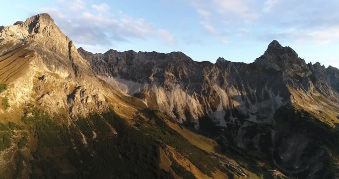 Cinematic view of alps mountain ridge and summit peak Zimba, Austria during sunrise. Drone filming moving sideways filming rocky mountains and green valley with hut cabin.