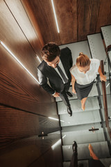 Top view full length smiling unshaven male going with cheerful lady while talking. They reflecting in mirror