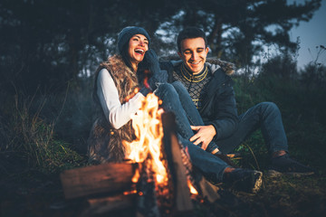 Pretty couple relaxing near bonfire in the forest at evening time
