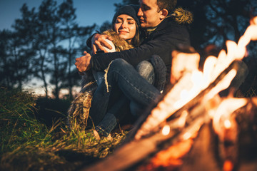 Pretty couple relaxing near bonfire in the forest at evening time