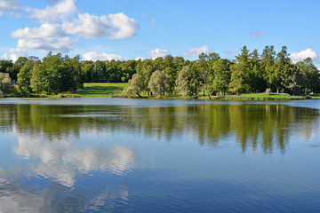 Fototapeta premium surface of a quiet blue lake reflecting the sky, white clouds and green forest on the opposite shore on a Sunny summer day