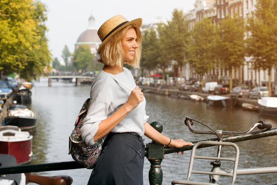 Happy traveler girl enjoying Amsterdam city. Smiling woman looking to the side on Amsterdam canal, Netherlands, Europe