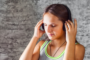 portrait of young teenager brunette girl with long hair listening music on headphones on gray wall background