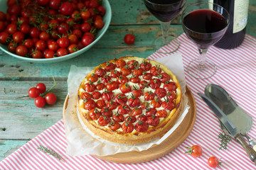 Tart, pie or cheesecake with cottage cheese and tomatoes, served with red wine on a wooden background.