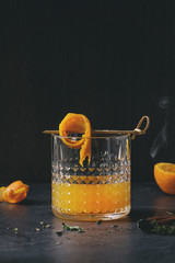Glass of Scotch Whiskey orange juice alcohol cocktail with swirled orange peel on skewer, thyme and...