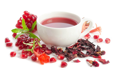 Parts of a pomegranate with pomegranate seeds and leaves, flowers, dry tea of carcade and full cup of tea isolated on white background