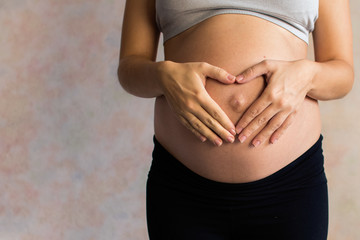 Pregnant Woman holding her hands in a heart shape on her baby bump. Pregnant Belly with fingers Heart symbol. Maternity concept. Baby Shower. toned