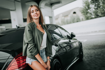 Portrait of outgoing sexy young lady situating near contemporary car outdoor. She expressing...