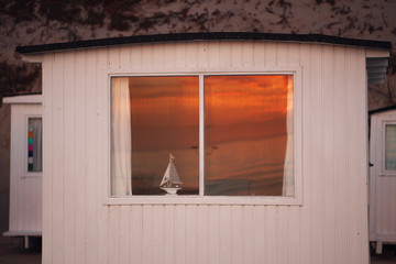Small white hut with a sailing boat in the window and sunset reflection. Løkken in North Jutland in Denmark, Skagerrak, North Sea