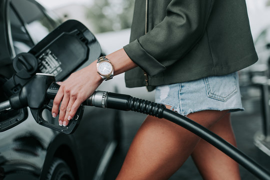 Close up female arm felling petrol line in gasoline inlet while standing near it. She wearing modern watch