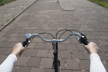 Naklejka na ściany i meble Handle bar on a bicycle seen from the point of view of the cyclist with street on the background and hands on the steering wheel