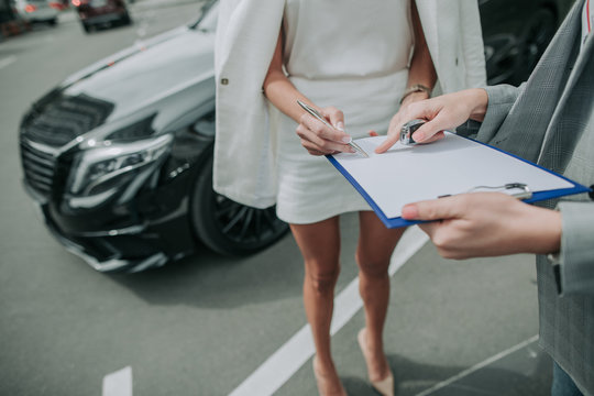 Putting signature here. Male consultant pointing finger where write young lady on document for buying modern automobile. She locating in white clothes opposite him