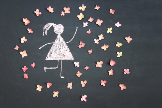 Chalk drawing woman icon surrounded by live pink flowers on chalkboard or blackboard. Women's day, feminism, girl power concept