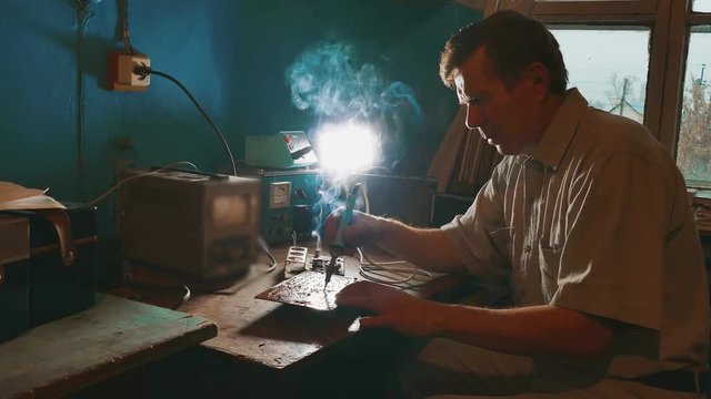 the old man repairs the chip radio technician smoke is coming repair soldering iron. Engineer lifestyle or technician repair electronic circuit board with soldering iron. man repair chips concept
