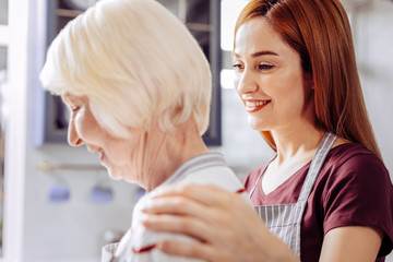 Smiling daughter. Peaceful young woman smiling and touching the shoulders of her senior mother while standing next to her