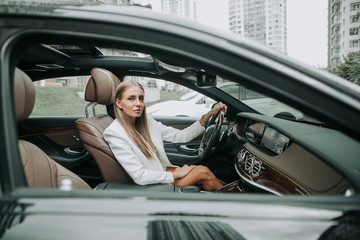 Portrait of serene young female sitting in modern car. She holding steering wheel. Orderly female going at work concept
