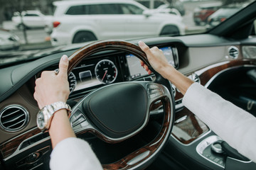 Close up woman hands keeping steering wheel of contemporary car. She wearing modern watch