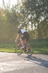 Active male athlete riding bicycles on an open asphalt road. Hills with green grass and the sunset