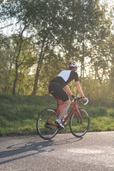 Fototapeta na wymiar Active male athlete riding bicycles on an open asphalt road. Hills with green grass and the sunset