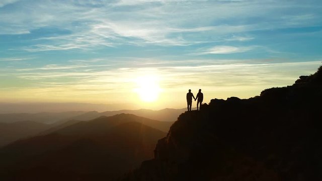 The couple standing on the mountain and watching to a beautiful sunrise