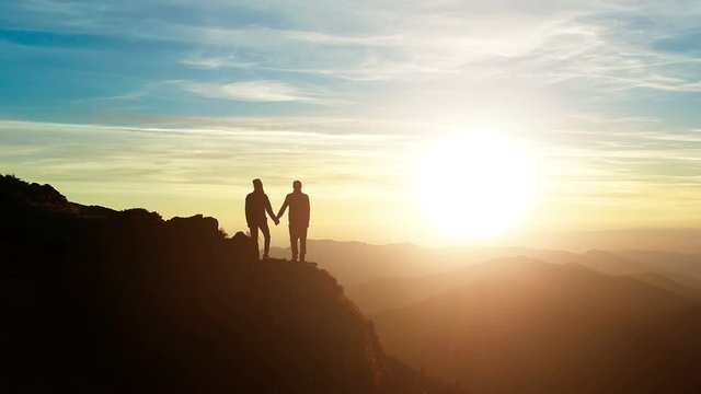 The couple standing on the mountain and watching to a sunset