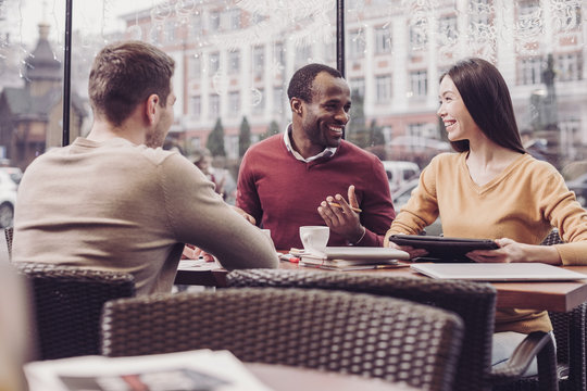 Friendly colleagues. Delighted international man actively gesticulating while talking to his partner