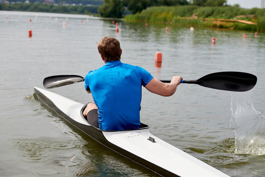 Rear view of athletic kayaker exercising in the water, he paddling on the lake in summer day