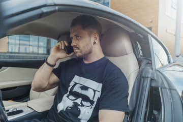 Man sitting behind the wheel of the black car and talking by mobile phone.