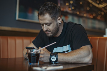 Young attractive man looking at mobile phone screen and drinking soda.