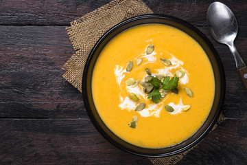 Pumpkin cream soup on dark wooden table.