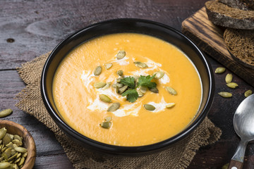 Pumpkin cream soup on dark wooden table.