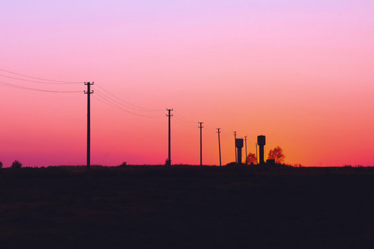 silhouettes of water towers and electricity poles on red sunset sky background - Powered by Adobe