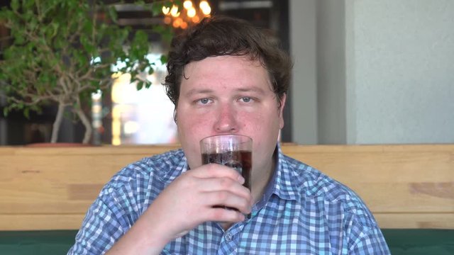 Fat man in the cafe or restaurant drinking cola