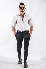 Portrait of brunette young man in white shirt and sunglasses, standing in studio shot isolated against white background. Full length photo