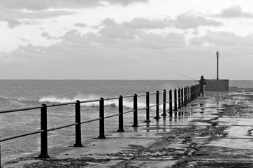 An unrecognizable man fishing on a pier in Port Alfred, South Africa. 