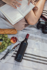 Cropped picture of girls legs reading a book while having a romantic picnic sitting in a city Parc and drinking wine with fruit and waiting for her boyfriend. Relaxing outdoors during summer holidays