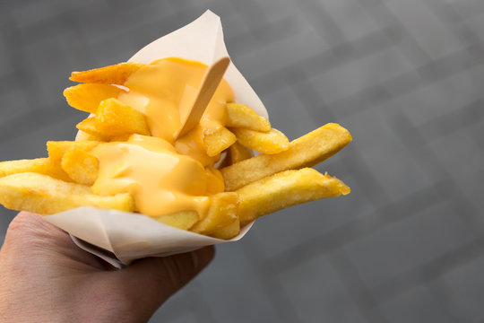 Man's hand holds a paper cone with french fries and creamy cheese as topping