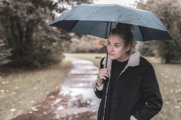 A young woman with an umbrella is waiting for better weather