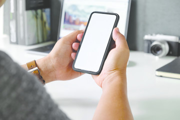 Cropped shot a man's hand holding blank screen mobile phone on desk.