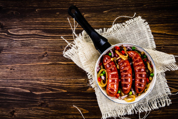 Grilled sausages with vegetables in pan on wooden table
