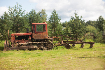 Fototapeta na wymiar Old farm tractor in pines and fir trees on the fringe