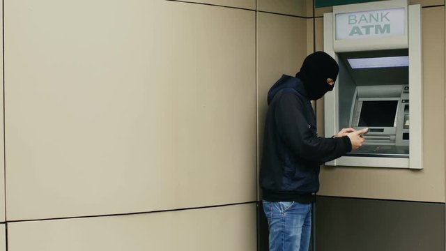 Hacker or thief with smartphone steals information or data from bank ATM