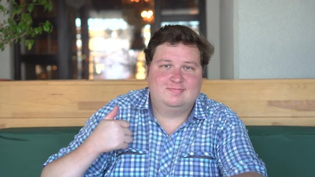 A handsome, fat man with big body shows thumbs up in the cafe or restaurant