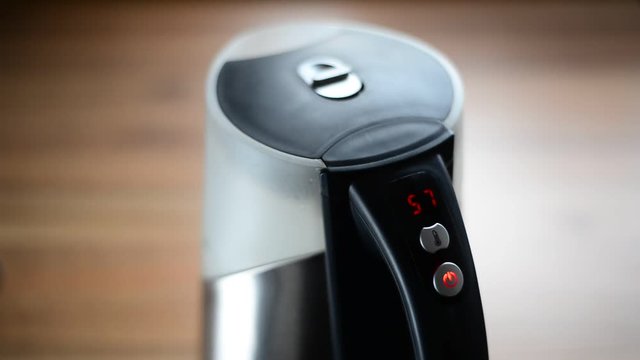 Boiling water in an electric cordless kettle with a digital display with red numbers.
