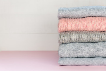 Fototapeta na wymiar Four grey and one pink folded knitted jumpers laying on pastel pink surface. Minimal concept. Autumn, fall, winter, spring fashion. Copy space. Fashion, lifestyle blogger. Pop of color.