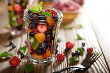 Assorted berries in mason jar on kitchen wooden table with fork aside