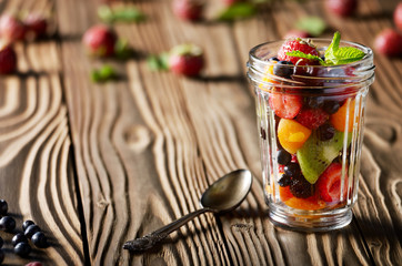Assorted berries in mason jar on kitchen wooden table with spoon aside
