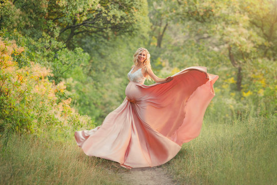 a sweet spring pregnant girl with light curly hair dances in the woods, is dressed in a delicate long elegant flowing pink dress with a white lace top, smiles into the camera and hugs her tummy. art